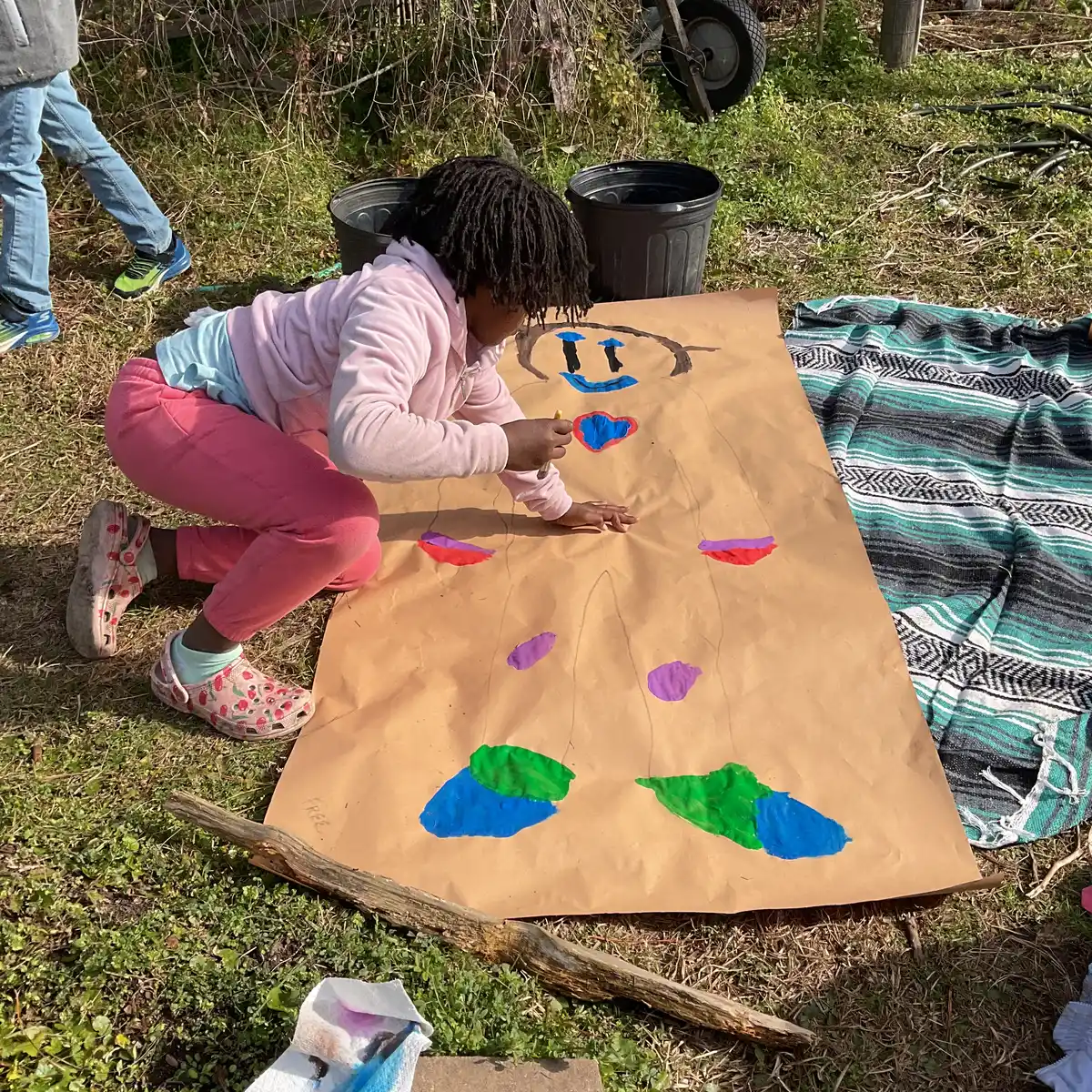 A student painting a colorful nature scene on butcher paper outdoors