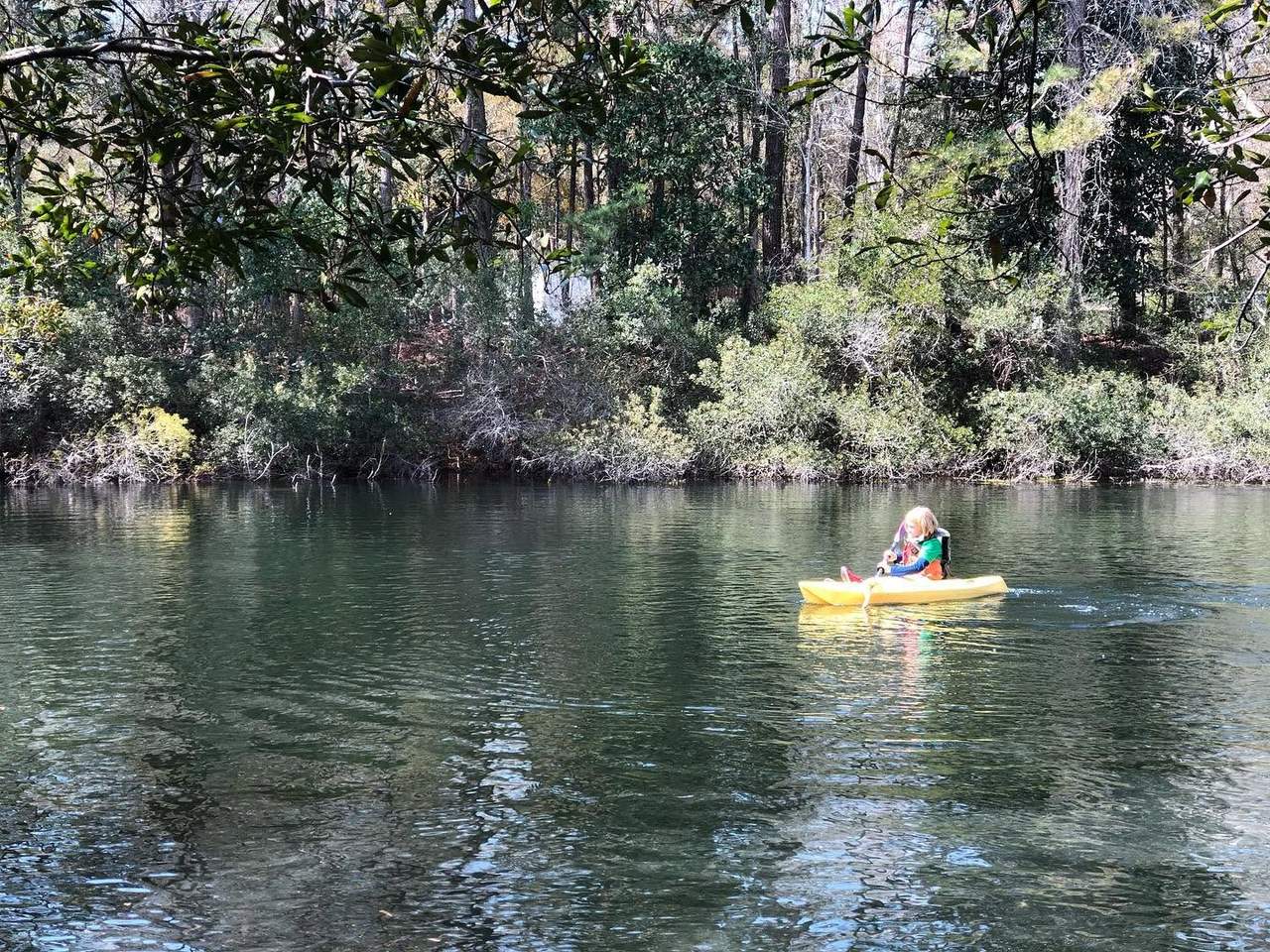 A camper paddling a kayak across the pond toward the tree-lined shore